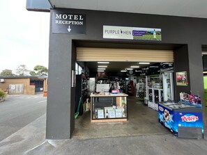 Een receptie van een motel met een bord waarop 'Motel Receptie' en 'Purple Hen' staan, eilandproducten en handwerk.