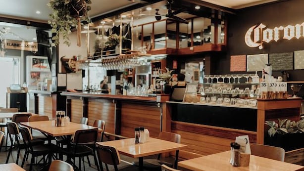 A restaurant interior with wooden tables and chairs, a bar area with a Corona sign, and various kitchen utensils on display. - San Remo Hotel Motel (San Remo)