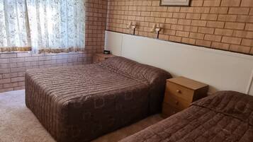 Een kamer met twee bedden, een bakstenen muur, een lijst met een afbeelding en een raam met gordijnen.