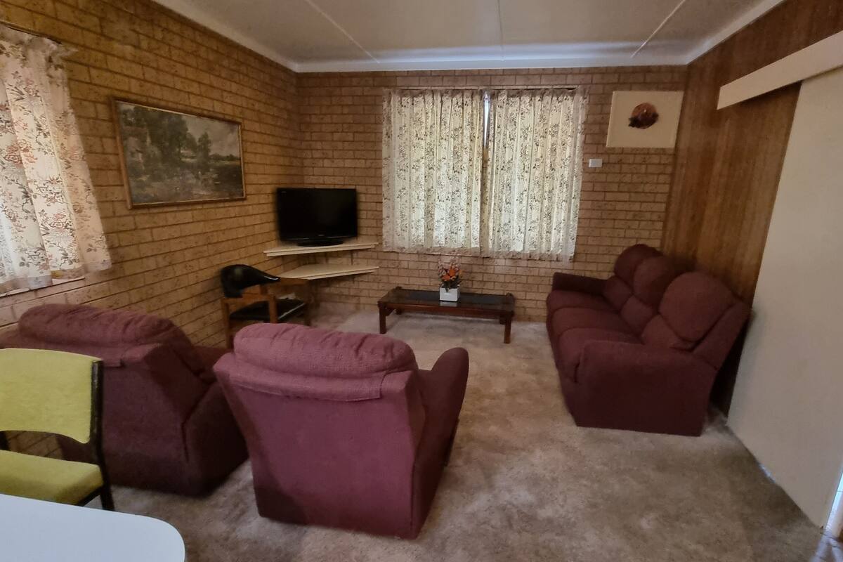Een woonkamer met bakstenen muren, een televisie op een meubelstuk, een bank, een stoel en een kleine tafel met een bloevas.