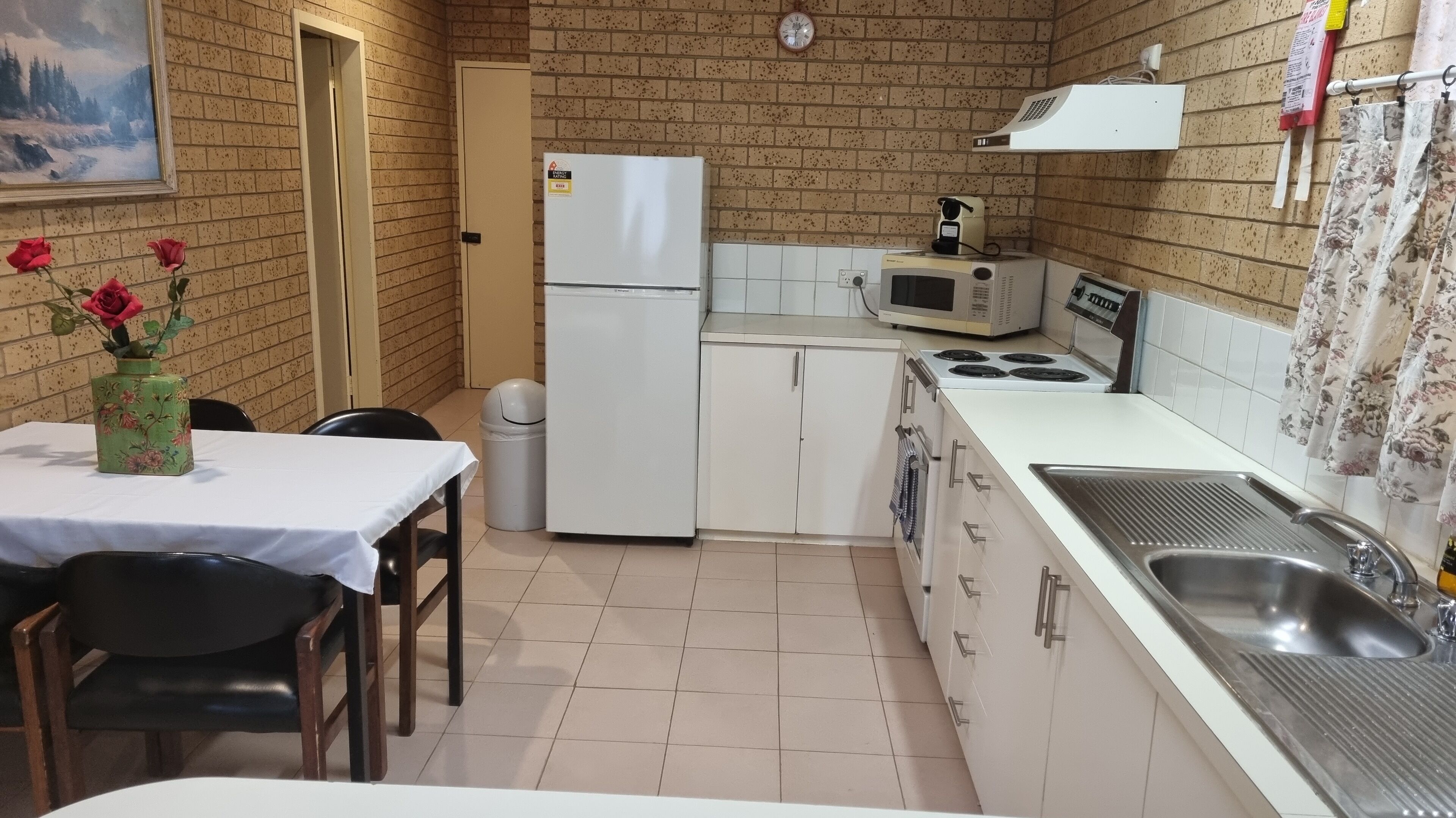 A compact kitchen with a refrigerator, microwave, stove, sink, and a dining area with a table and chairs.