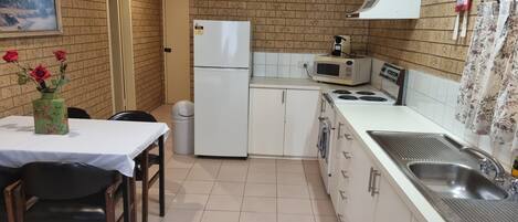 A compact kitchen with a refrigerator, microwave, stove, sink, and a dining area with a table and chairs.