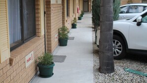 Fila de edificios de ladrillo de una sola planta con espacios de estacionamiento numerados, plantas en macetas y un coche blanco estacionado en la calle.