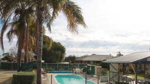 Una piscina con zona vallada, rodeada de palmeras y un área de estar techada.