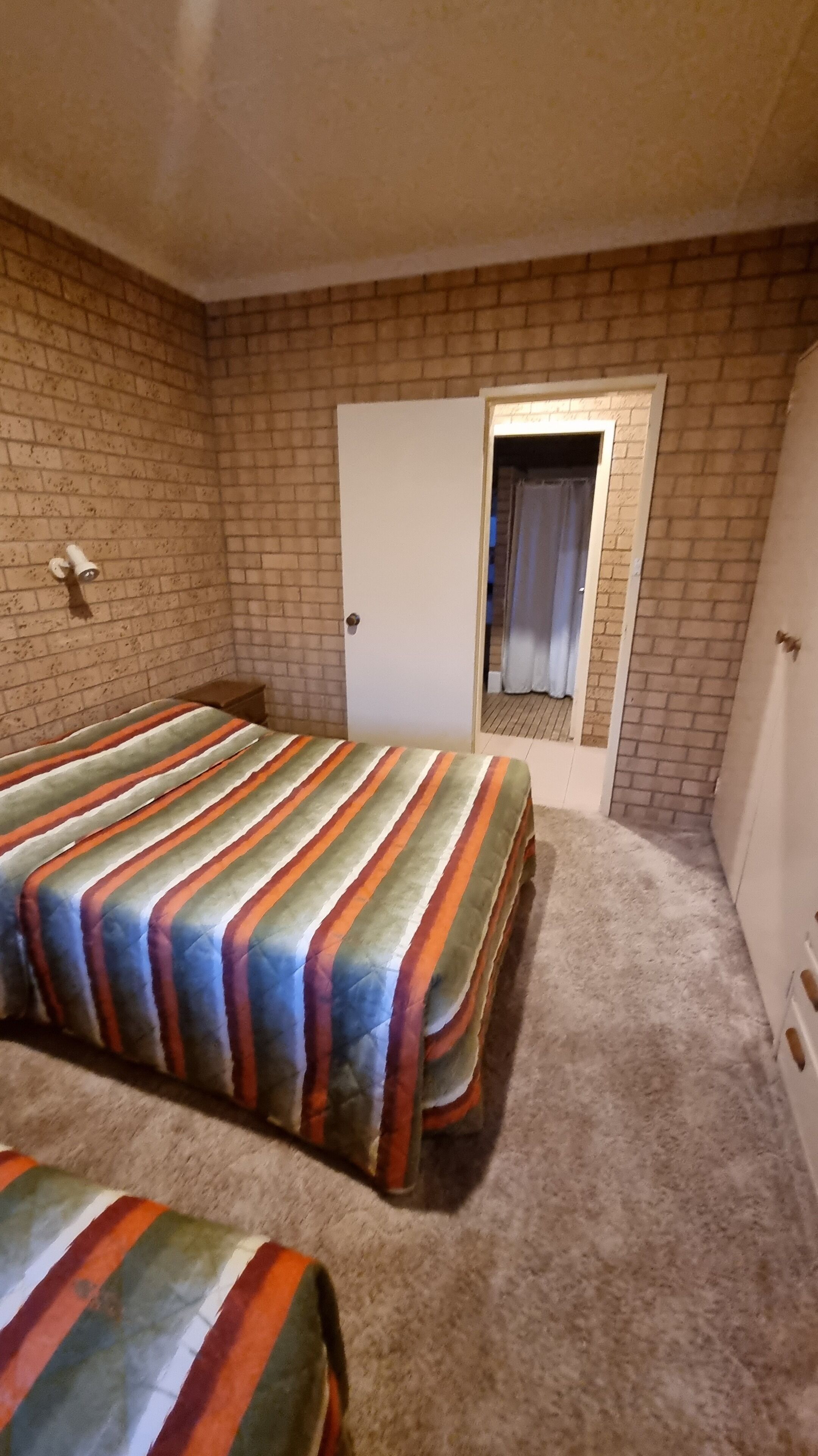 Un dormitorio con pared de ladrillo, una puerta y una ventana con cortinas.