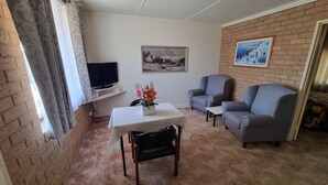 Una sala de estar con televisor, dos sillones, una mesa con un jarrón de flores y un cuadro en la pared.