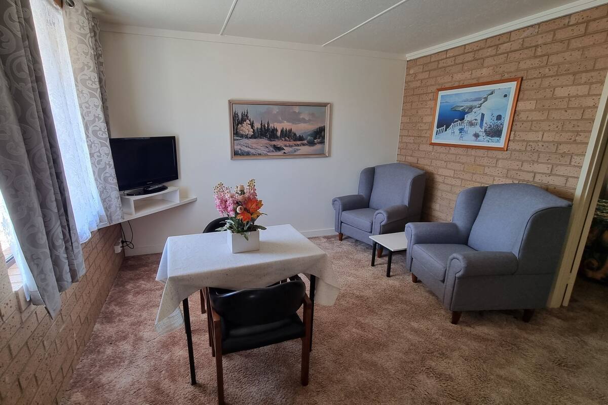 Een woonkamer met een televisie, twee fauteuils, een tafel met een bloevas en een schilderij aan de muur.