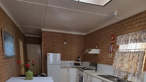 Cocina compacta equipada con refrigerador, estufa, microondas y pileta. Cuenta con un comedor con mesa y sillas, y un ventanal con cortinas.