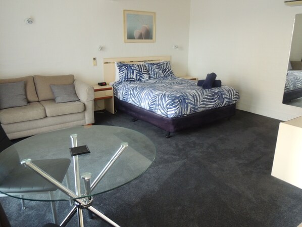 A bedroom with a bed, a sofa, a glass table, and a nightstand.