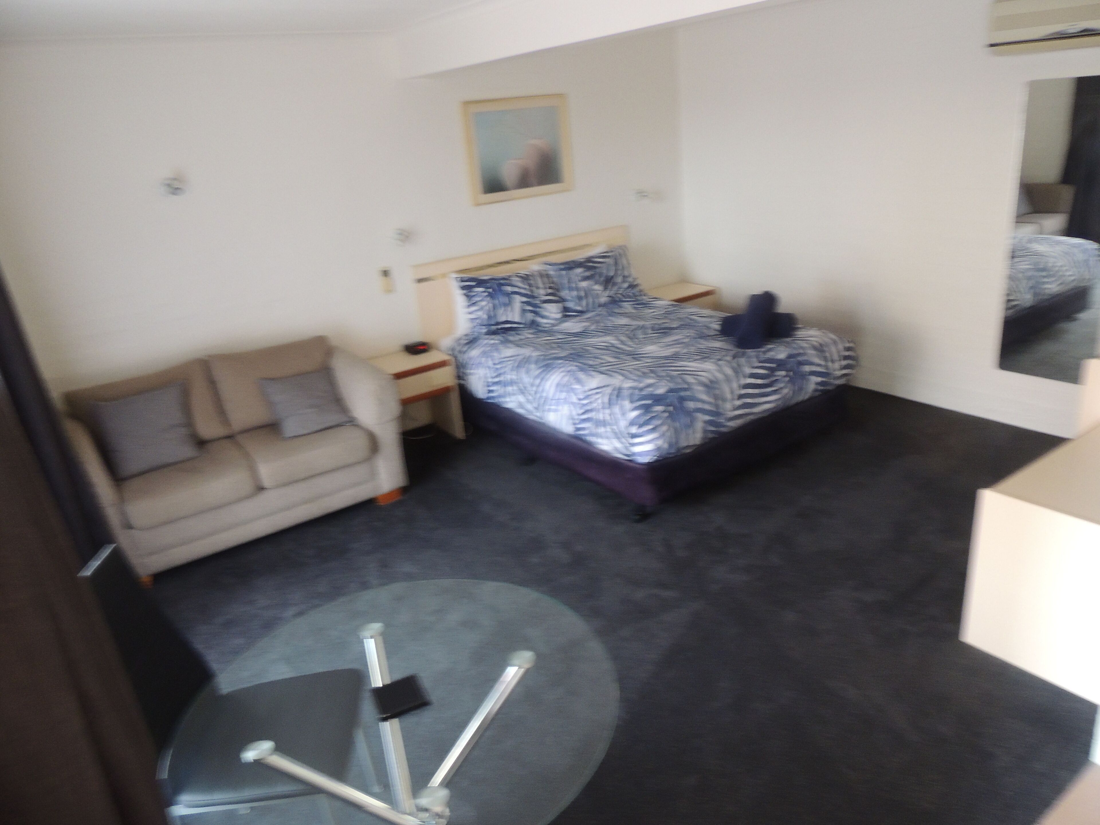 A hotel room with a bed, a sofa, a small table, and a mirror.