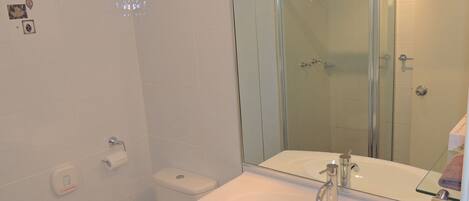 Un baño con lavamanos blanco, cabina de ducha de vidrio y un inodoro.