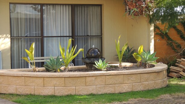 A landscaped garden with a circular stone border, a variety of plants, and a decorative stone fountain.
