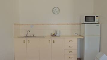 A compact kitchen with a sink, microwave, and a clock on the wall.