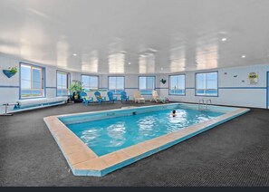 An indoor swimming pool with clear blue water, surrounded by lounge chairs and a view of the ocean through large windows. - Blue Seas Holiday Villas (Scamander)