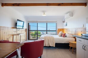 A compact room with a bed, a small table, a red chair, and a TV mounted on the wall. - Blue Seas Holiday Villas (Scamander)