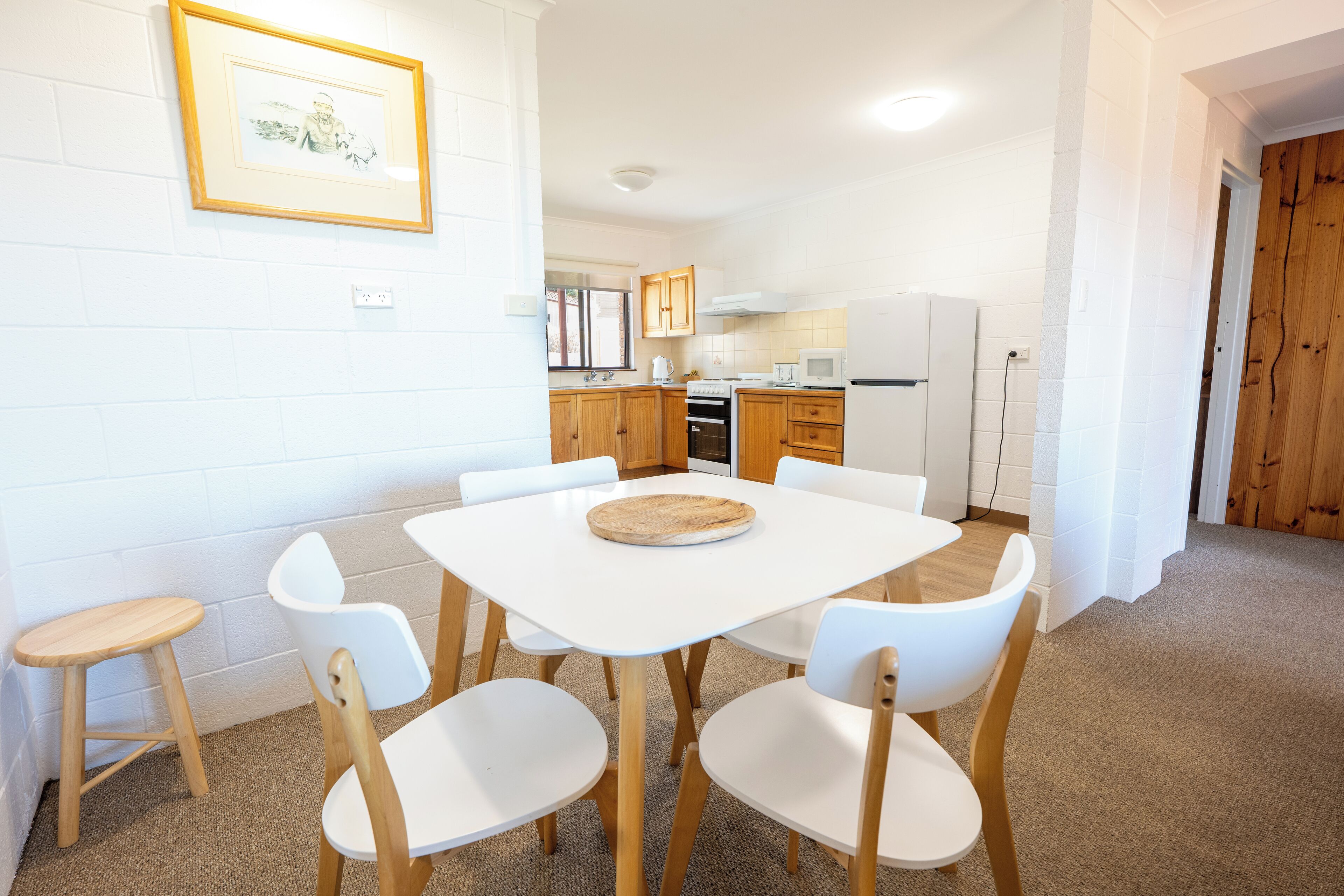 Een moderne keuken met witte kasten, een eettafel met stoelen en een foto in een lijst aan de muur.