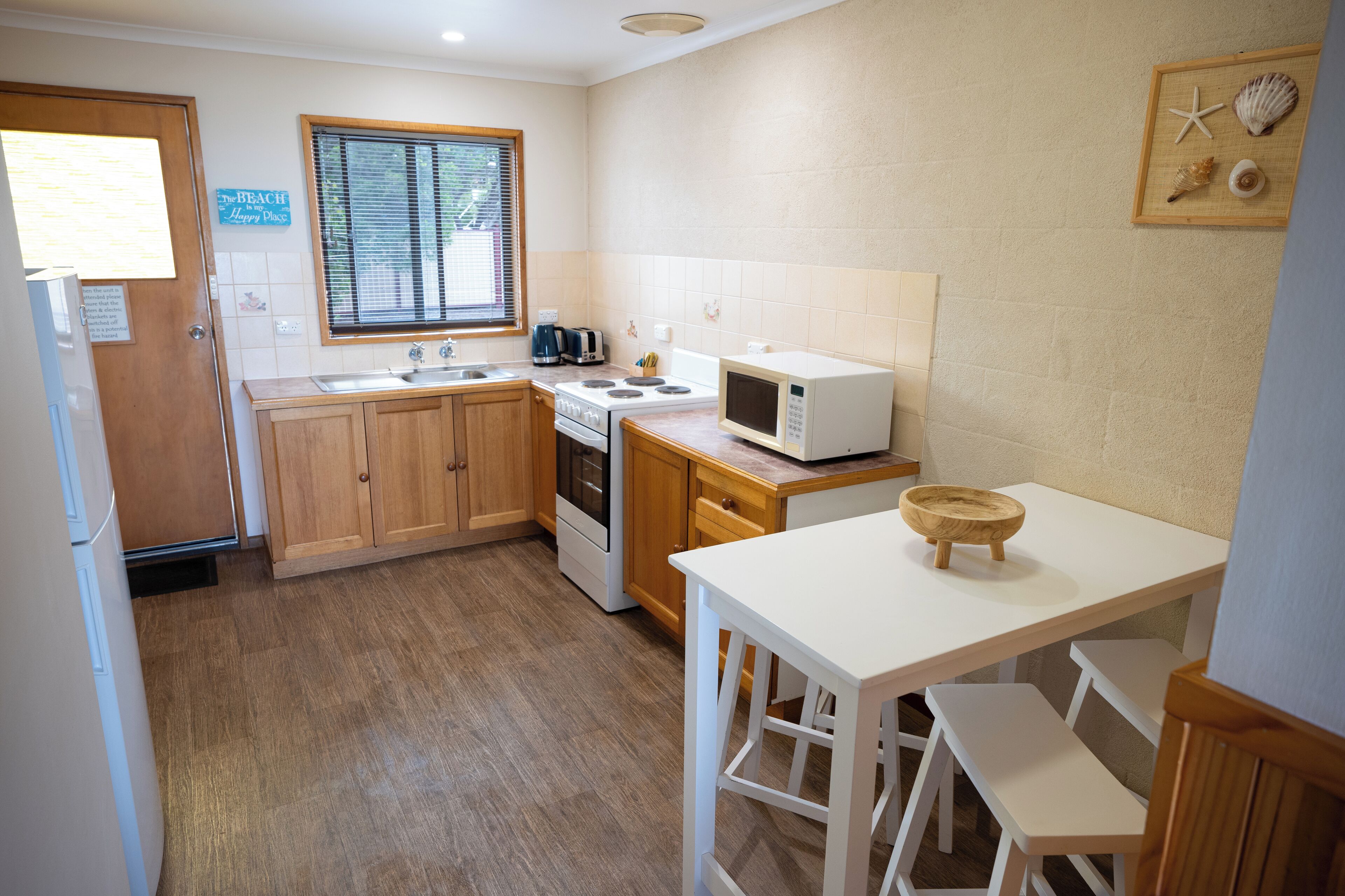 Una cocina compacta con armarios de madera, microondas, tostadora y lavamanos.