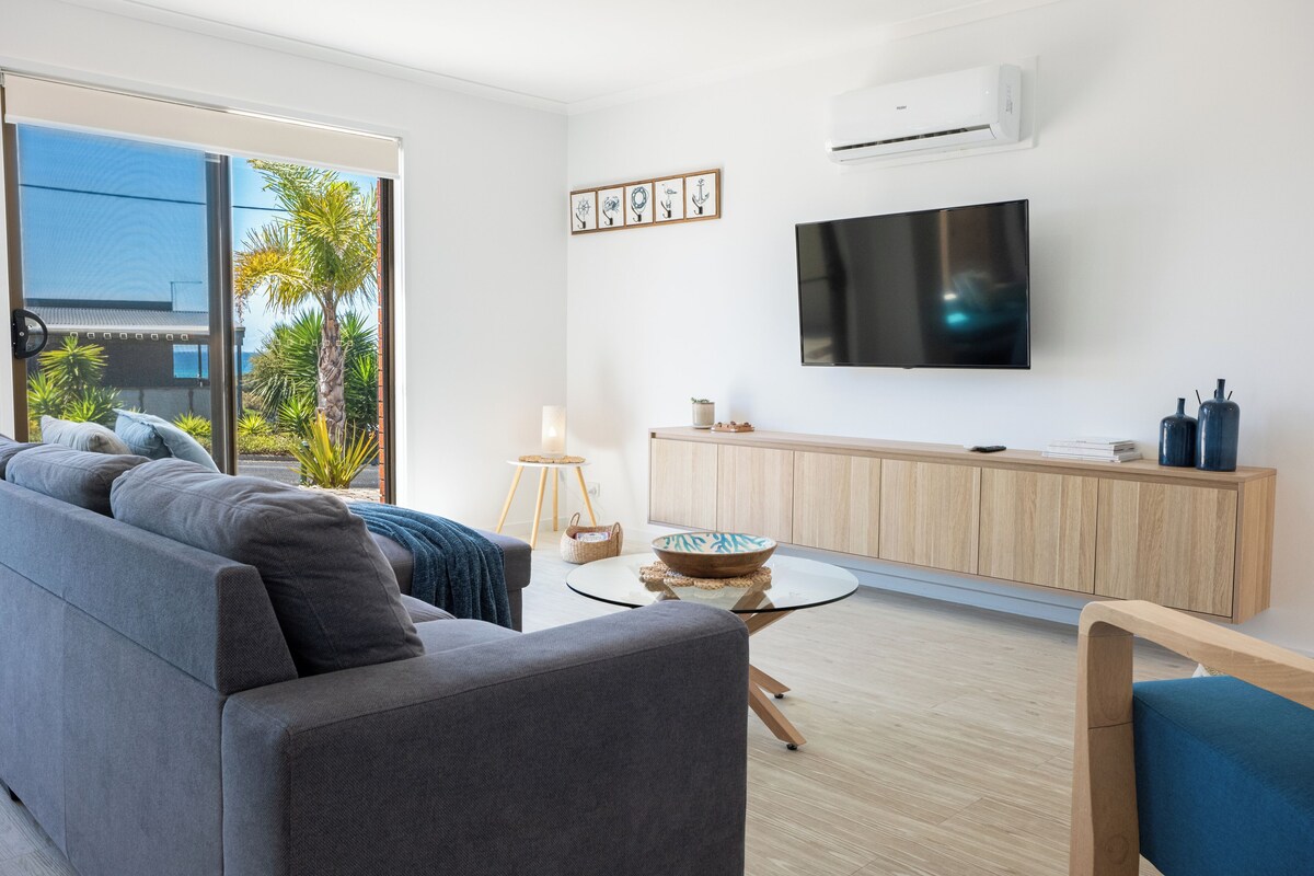 A modern living room with a grey sofa, a round coffee table, a TV on the wall, and a wooden cabinet.