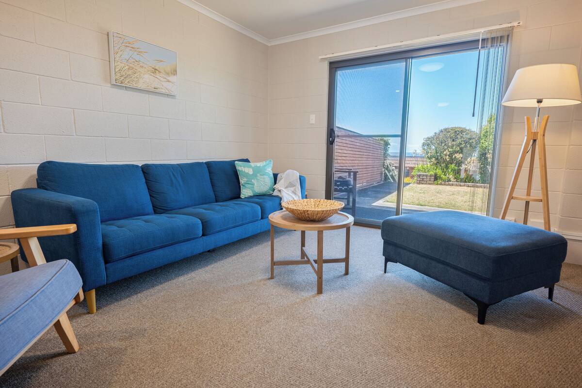A living room with a blue sofa, a small round table with a woven basket, and a floor lamp.