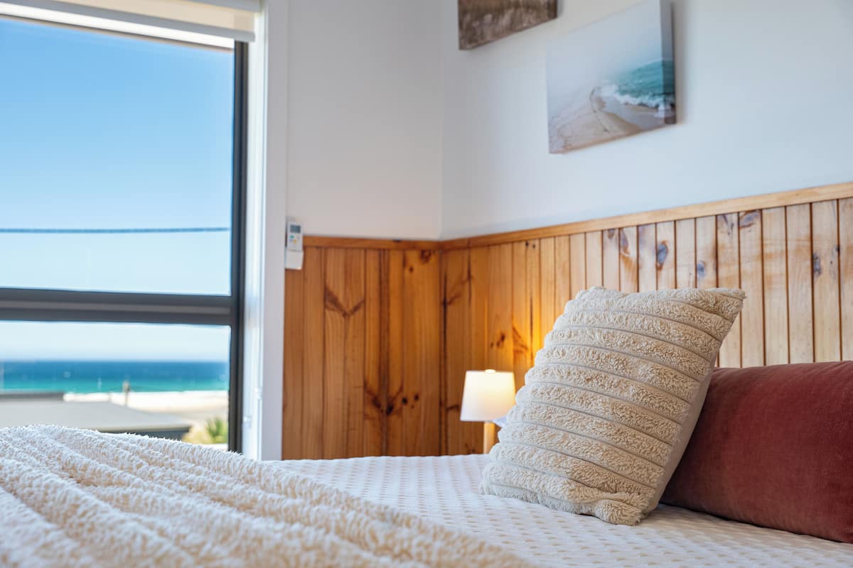 A bedroom with a wooden headboard, a white bedspread, a beige pillow, and a red pillow.
