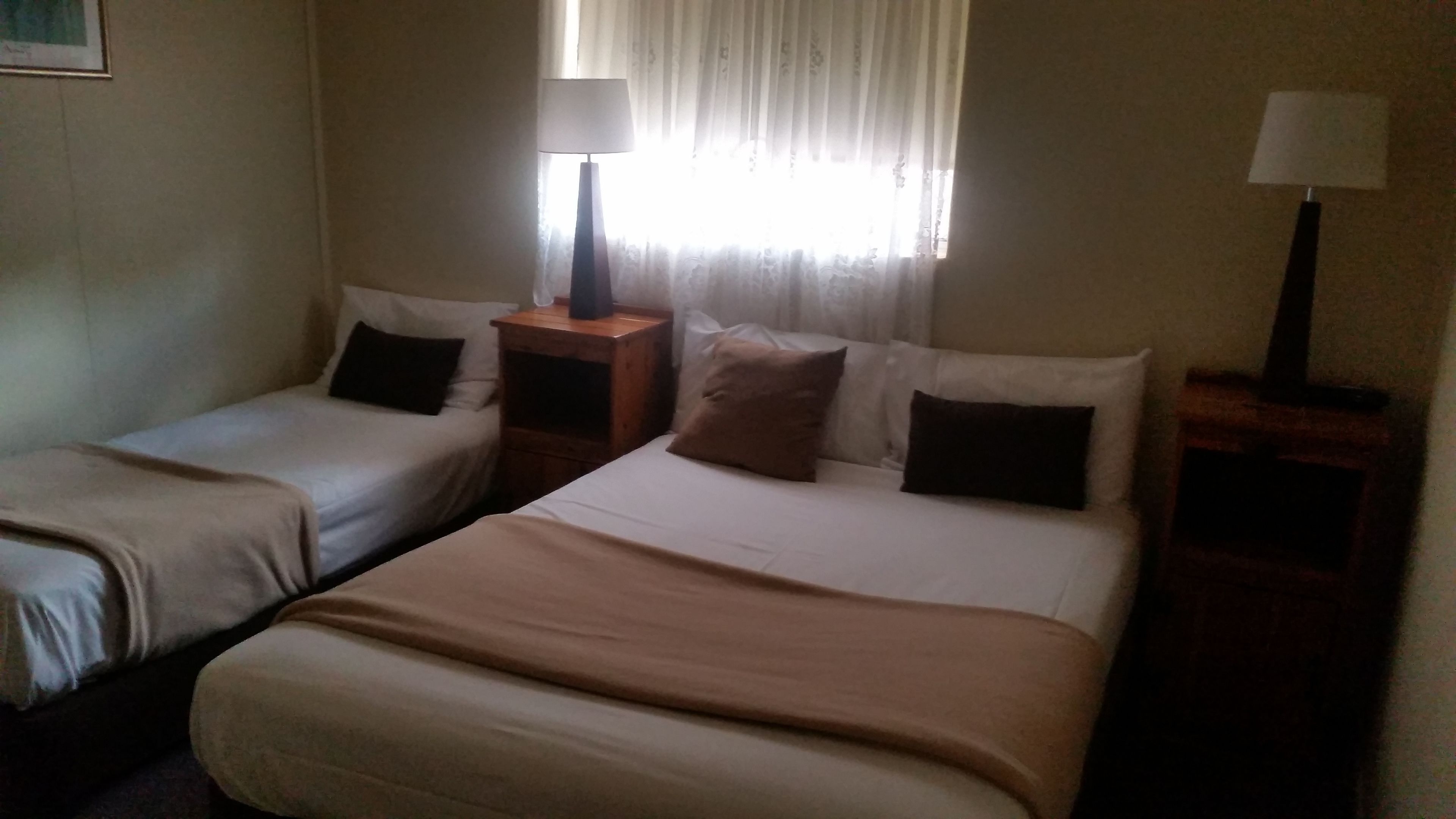 A hotel room with two single beds, a nightstand with a lamp, and a window with curtains.