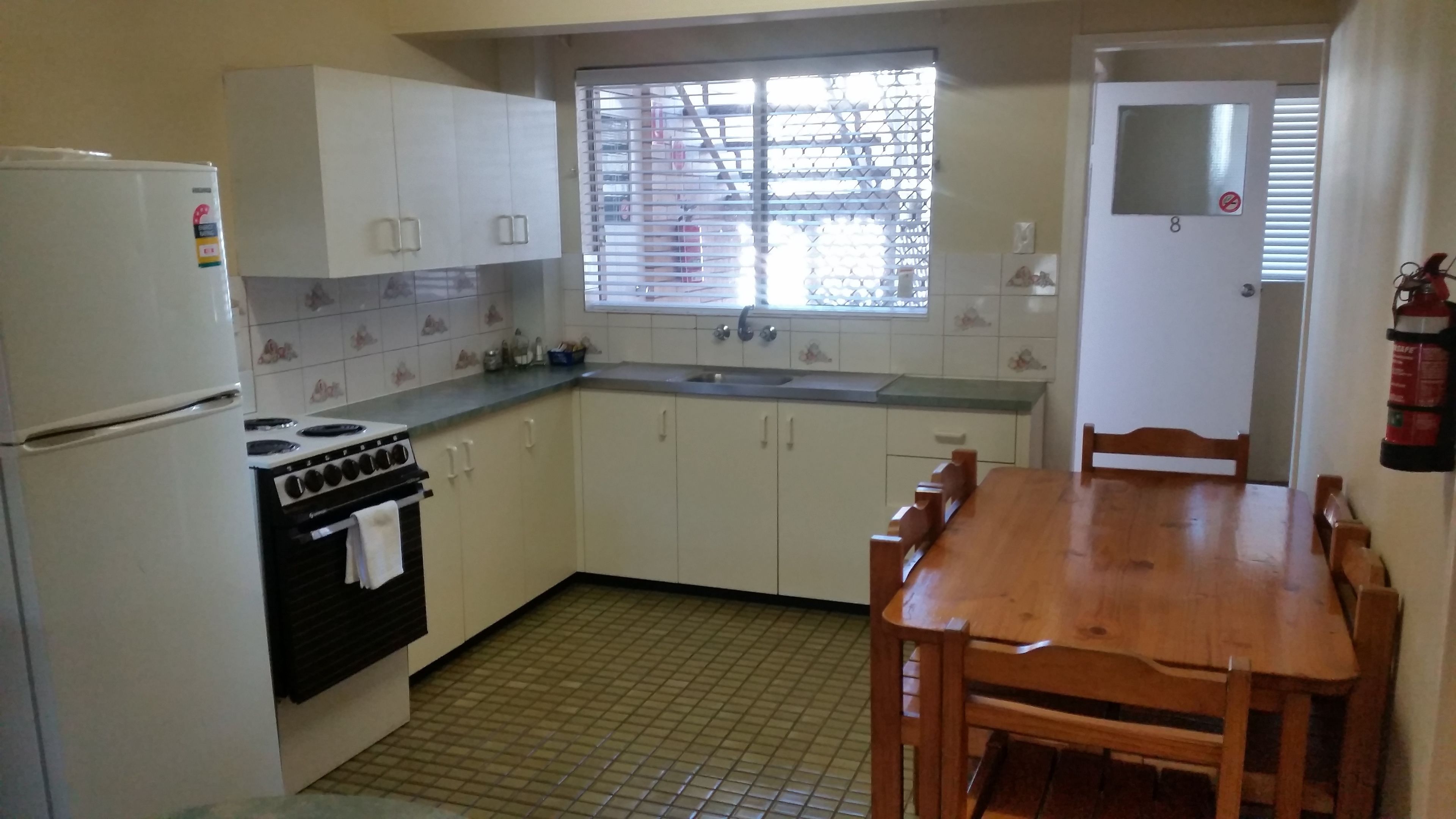 A compact kitchen with white cabinets, a stove, a refrigerator, and a wooden dining table.
