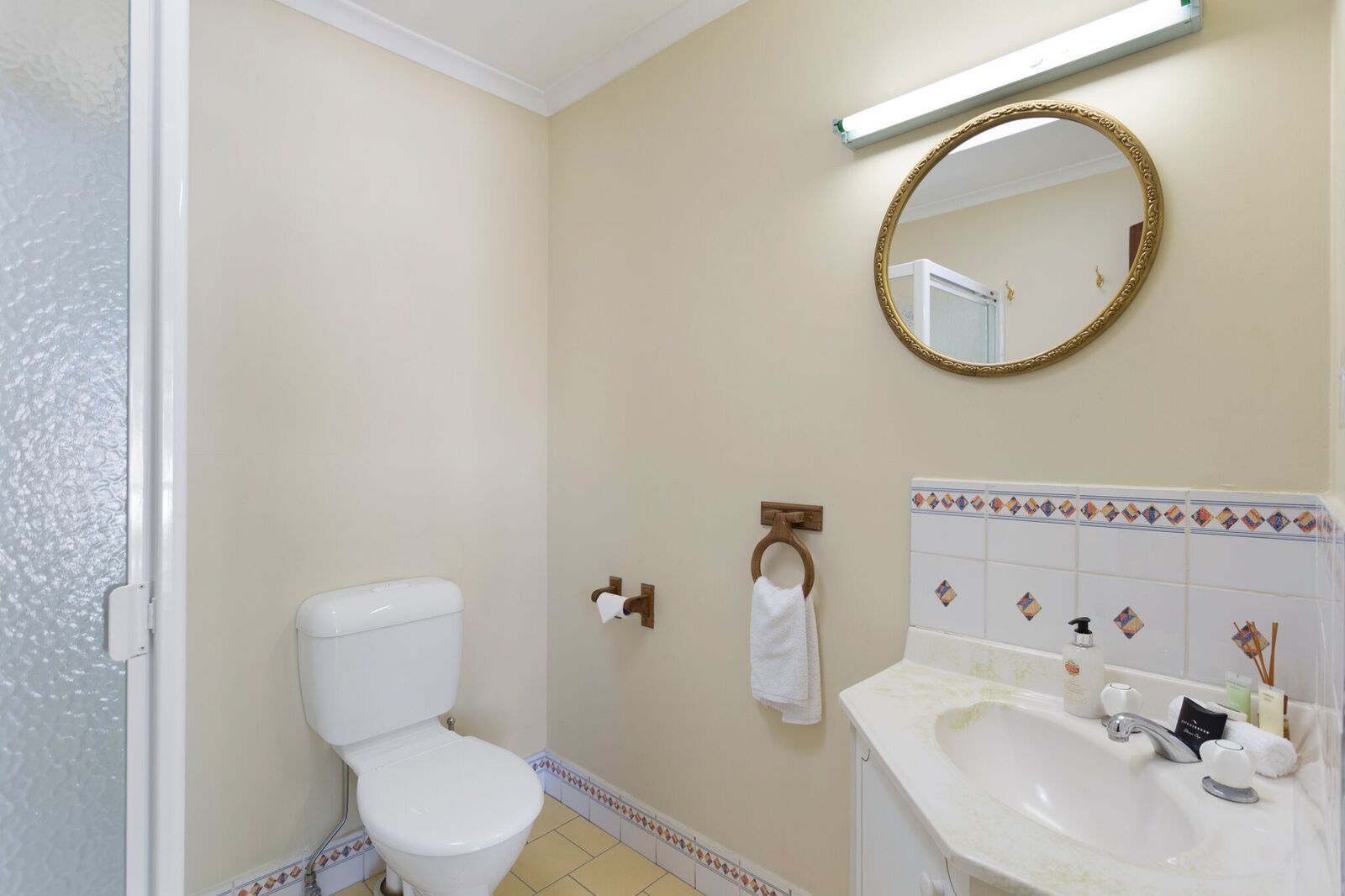A bathroom with a toilet, sink, mirror, and towel rack.