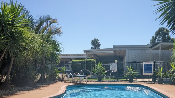 A swimming pool with clear blue water, surrounded by palm trees and a fenced area. - Kaputar Motel Narrabri (Narrabri)