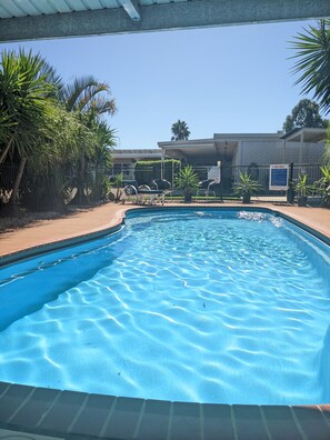 Piscina con agua azul cristalina, rodeada de palmeras y una zona vallada.