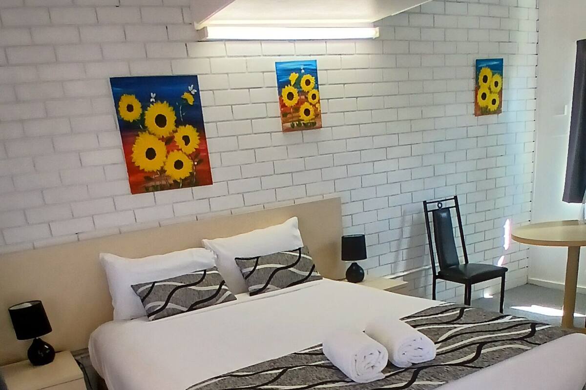 A hotel room with a large bed, a nightstand, a chair, a small table, and artwork on the walls.