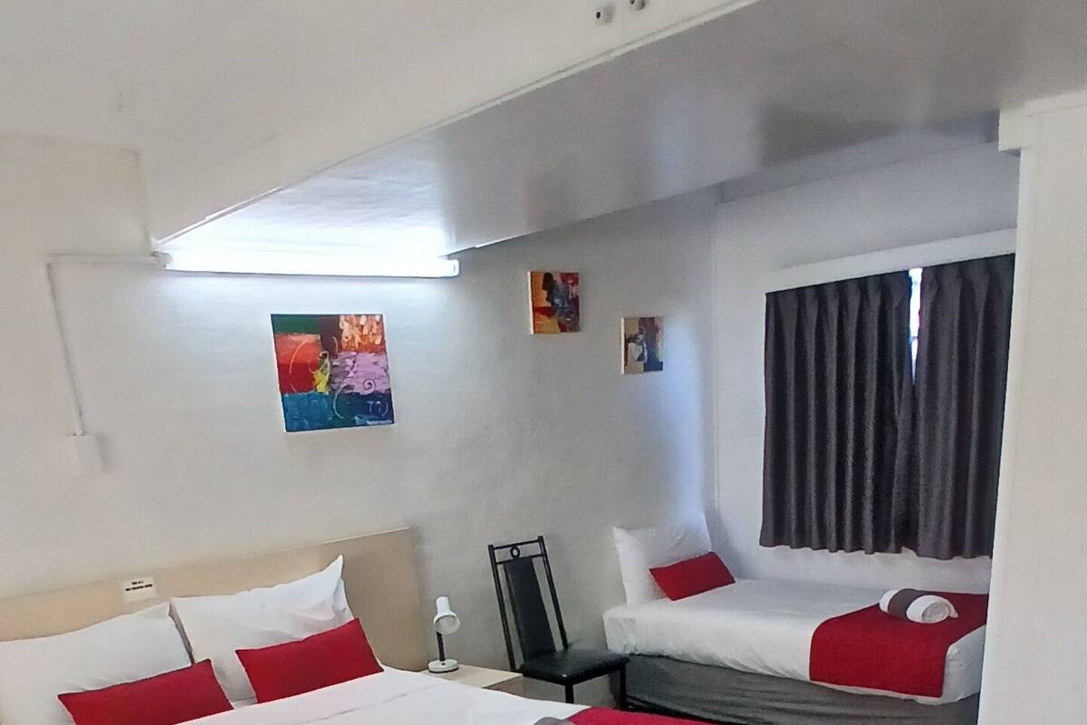 A hotel room with two beds, a desk, and a chair. There are two paintings on the wall.