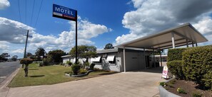 Un motel con área de estacionamiento techada, un letrero que indica habitaciones agotadas y cielo despejado.