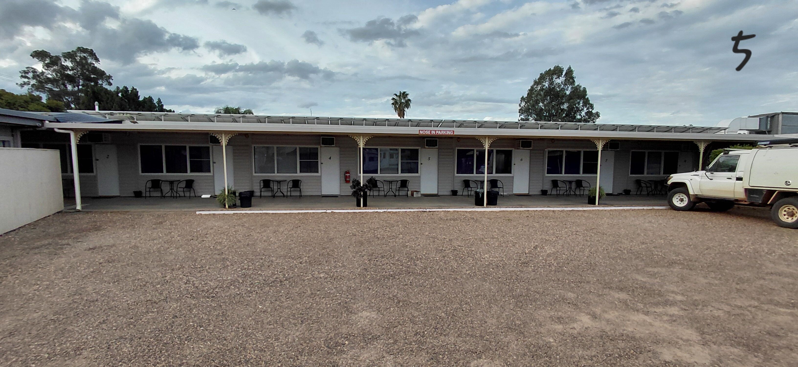 A building with a covered parking area, numbered rooms, and outdoor seating.