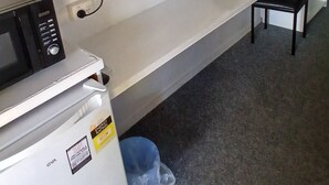 A kitchenette with a microwave, refrigerator, and a small trash bin. There is a flat-screen TV mounted on the wall, a small potted plant, and a chair. - Kaputar Motel Narrabri (Narrabri)