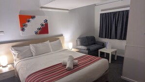 A modern hotel room with a large bed, a bedside table, a chair, and a window with curtains. - Kaputar Motel Narrabri (Narrabri)