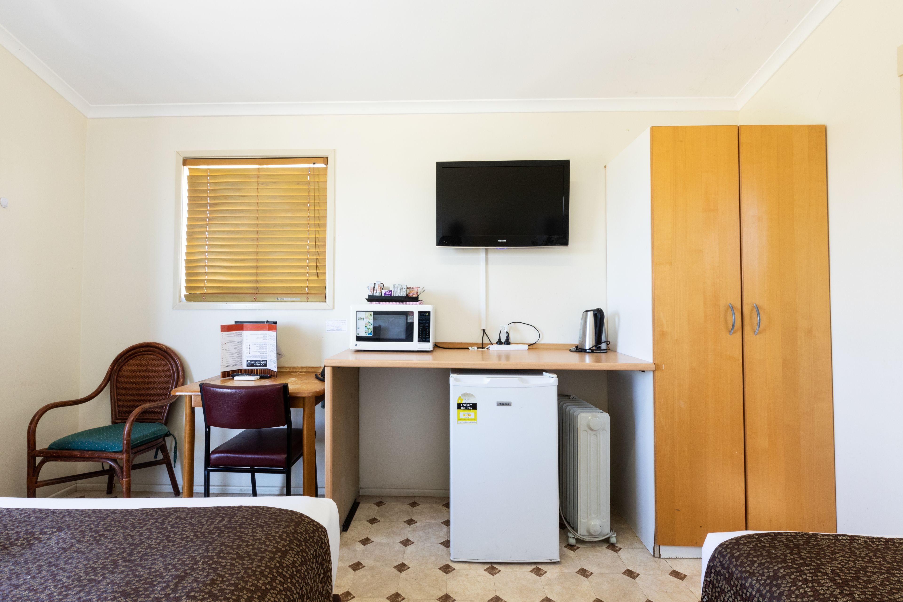 A compact hotel room with a bed, a desk with a microwave, a refrigerator, a television, and a wardrobe.