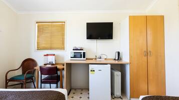 Habitación de hotel compacta con cama, escritorio con microondas, refrigerador, televisión y armario.