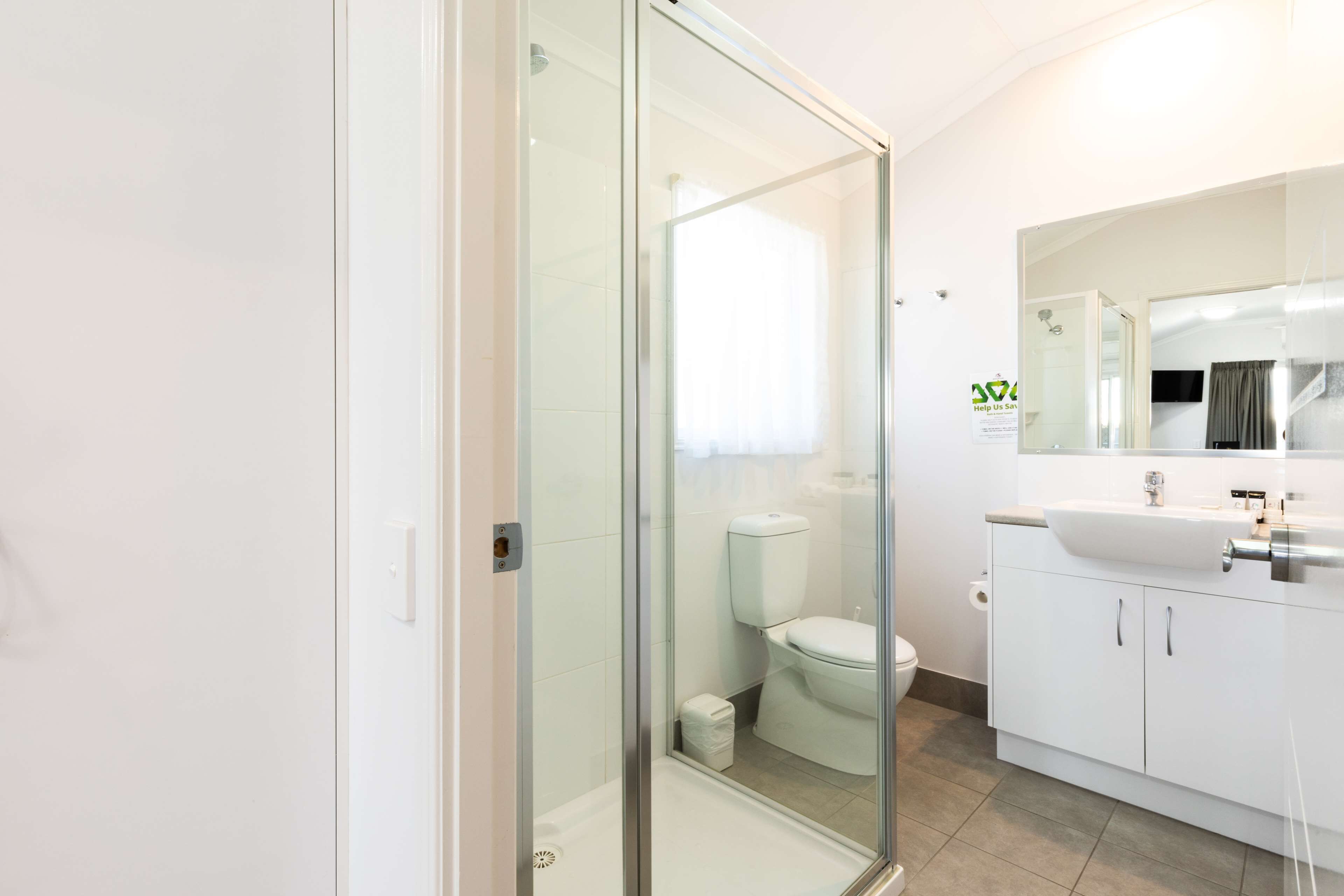 A modern bathroom with a glass shower enclosure, a toilet, and a sink with a mirror above it.