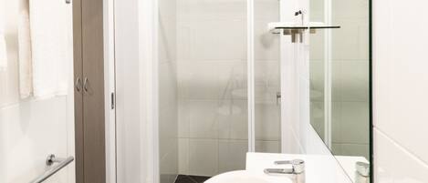 A modern bathroom with a white sink, a glass shower enclosure, and a visible door leading to another room.