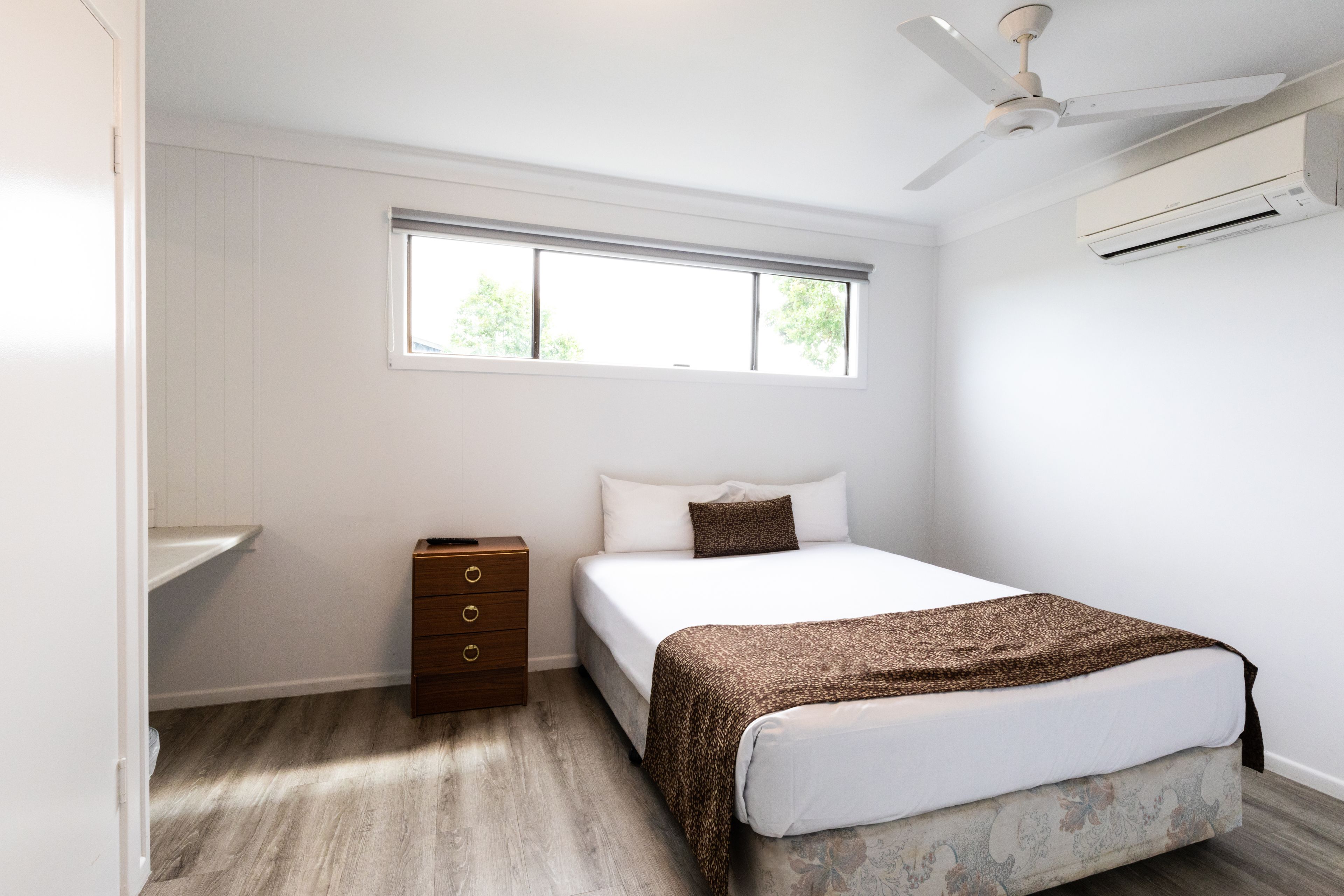 A bedroom with a bed, a window, a ceiling fan, and an air conditioning unit.