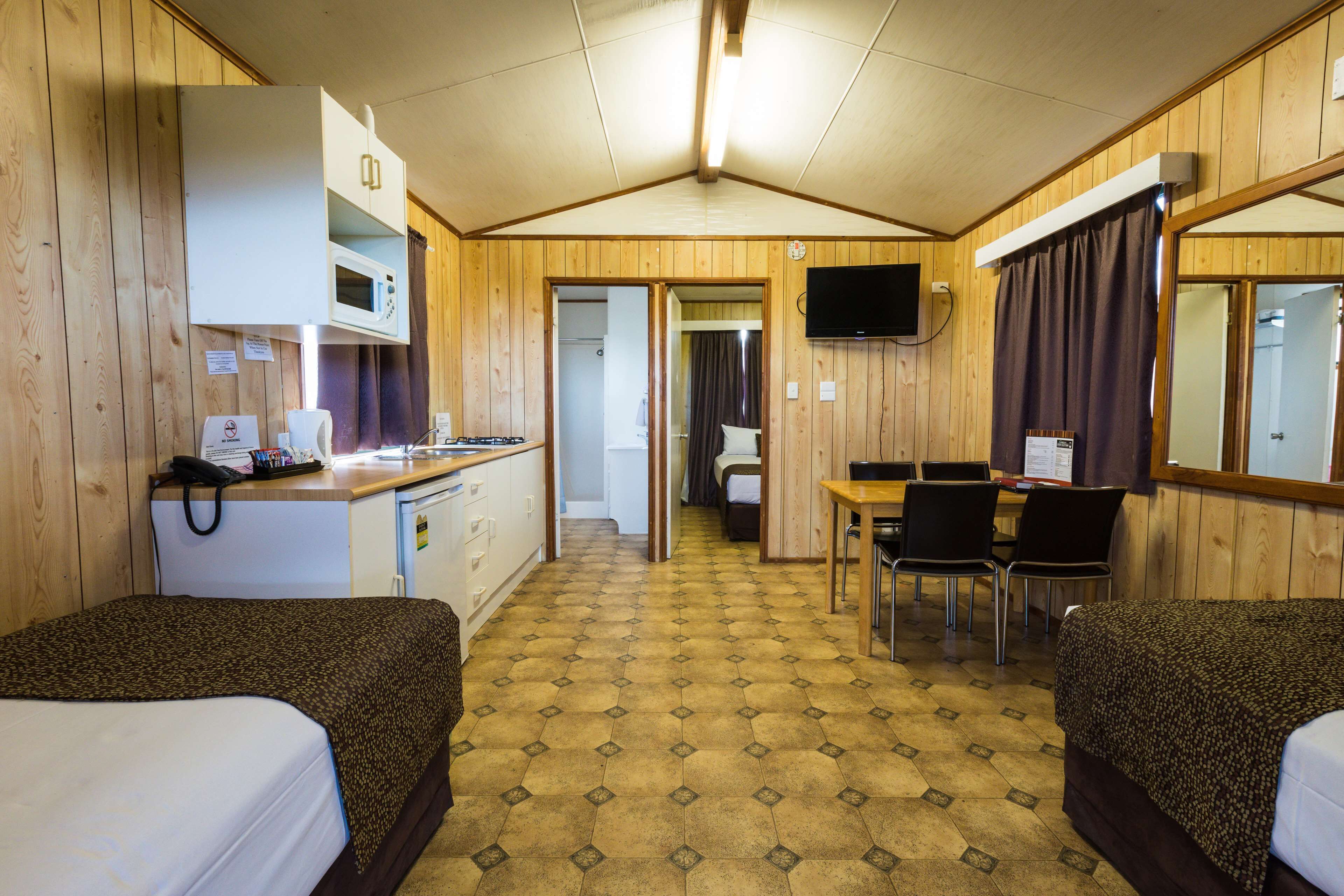 A room with two beds, a kitchenette, a dining area, and a TV mounted on the wall.