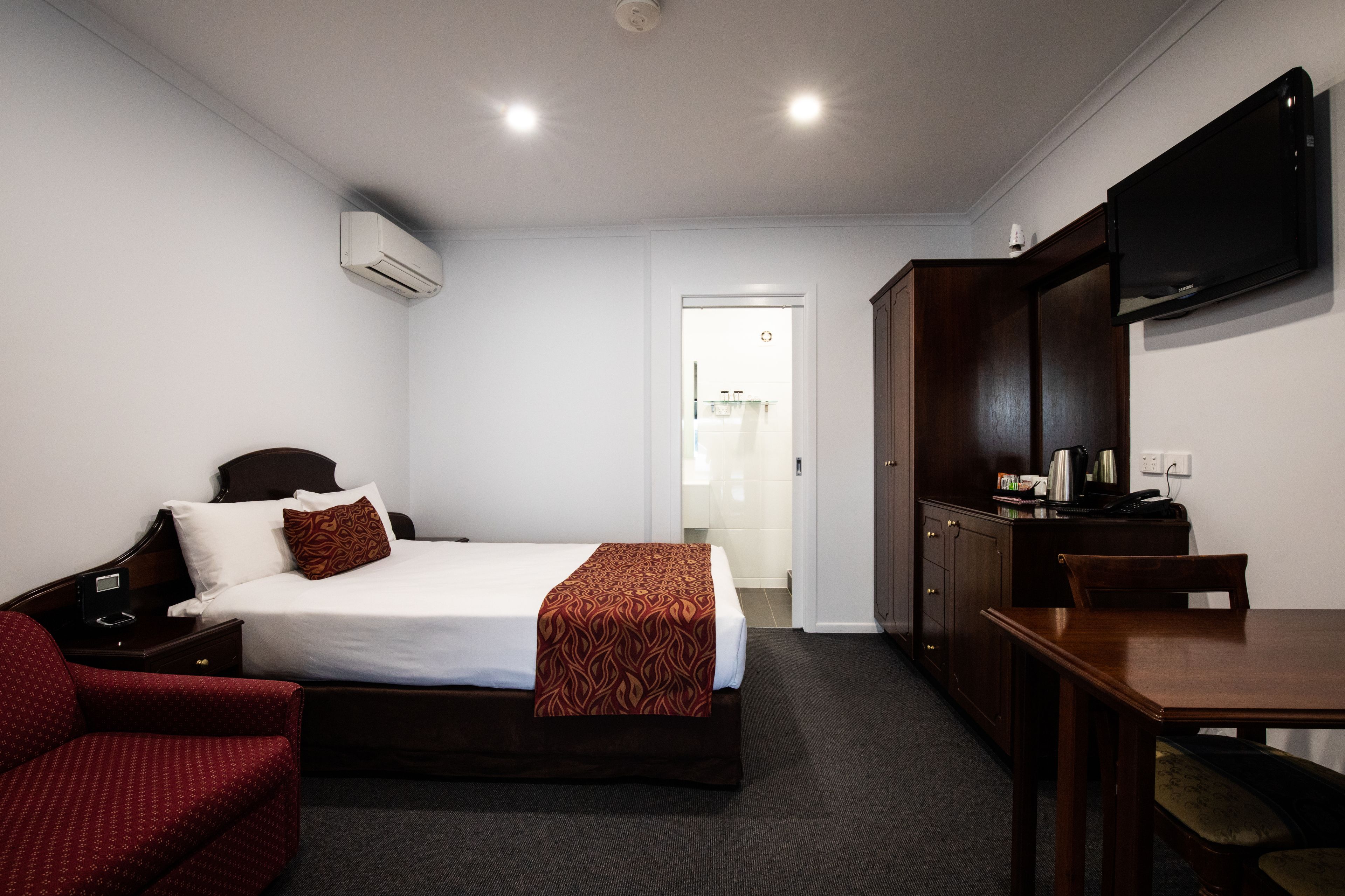 Quarto de hotel com uma cama, uma escrivaninha, uma cadeira, uma televisão e um aparelho de ar condicionado.