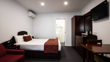 Quarto de hotel com uma cama, uma escrivaninha, uma cadeira, uma televisão e um aparelho de ar condicionado.