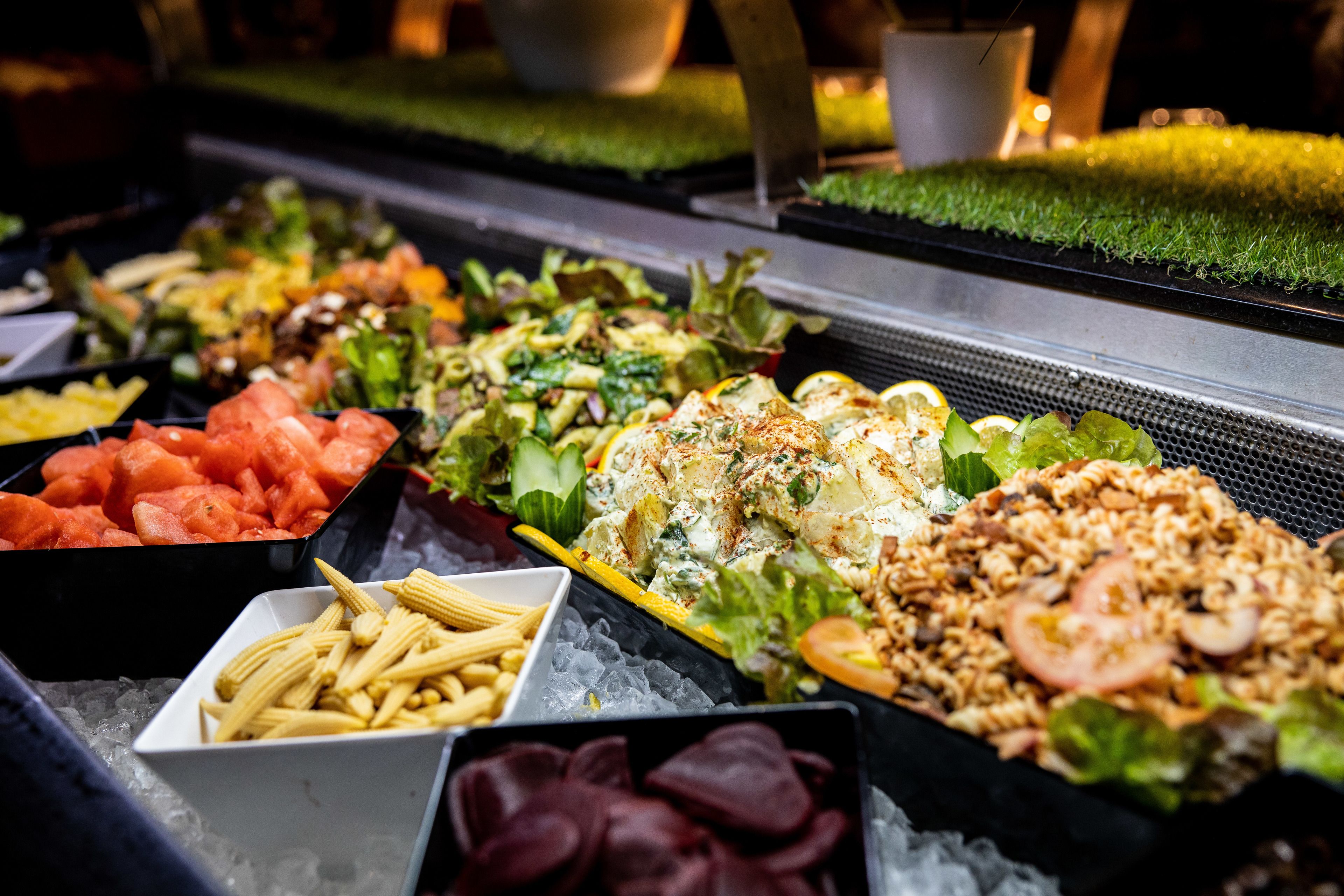 A buffet with various food options including pasta, salads, and fruits.