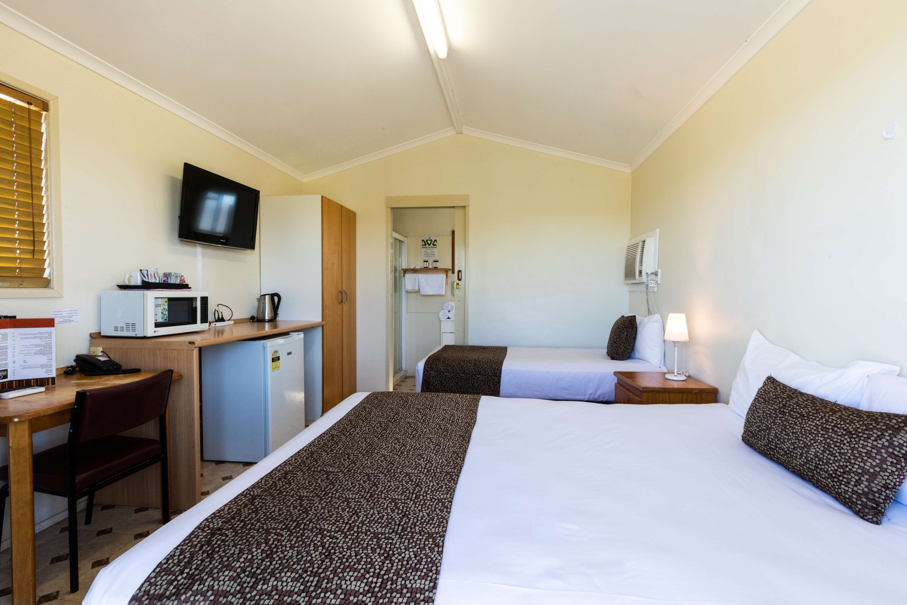 A hotel room with two beds, a desk with a microwave, a TV, and a small refrigerator.