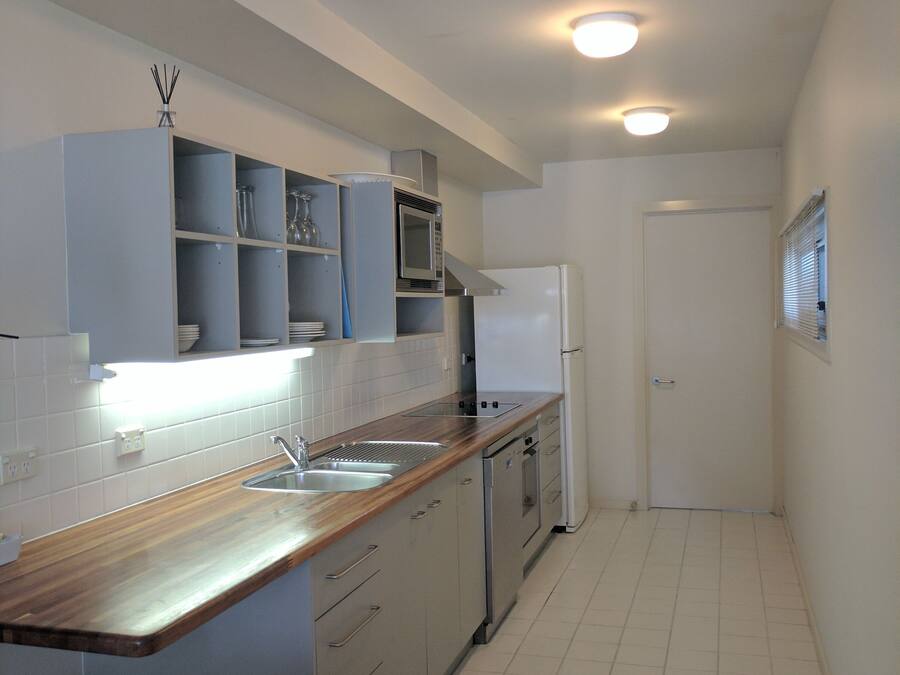 A modern kitchen with white cabinets, a wooden countertop, a stainless steel sink, and a white refrigerator.