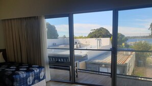 Une chambre avec une grande fenêtre, un lit et une vue sur un immeuble doté d’un toit plat.