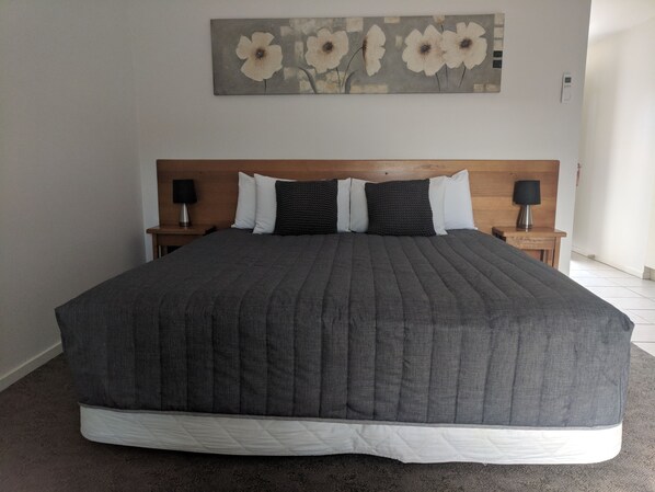 A large bed with a grey quilt, two bedside tables with lamps, and a floral artwork on the wall.