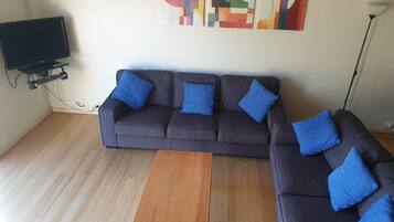 A living room with a grey sofa, blue cushions, a wooden coffee table, and abstract wall art.