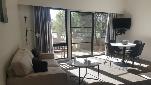 Une chambre d’hôtel moderne équipée d’un canapé, d’une petite table ronde, d’une télévision et d’un balcon avec du mobilier d’extérieur.